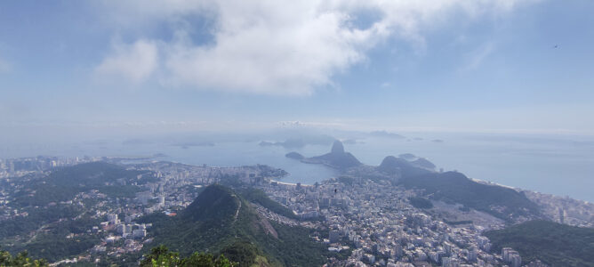 Do alto do Corcovado, a cidade se descortina: Flamengo à esquerda, Botafogo e o Pão de Açúcar ao centro, e Copacabana se estendendo à direita.